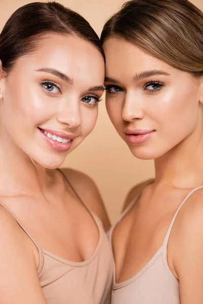 Dos mujeres sonrientes con rostro natural y piel perfecta mirando a la cámara aislada en beige — Stock Photo