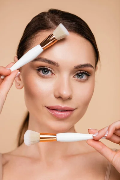 Portrait of pretty woman with perfect skin holding cosmetic brushes isolated on beige — Stock Photo