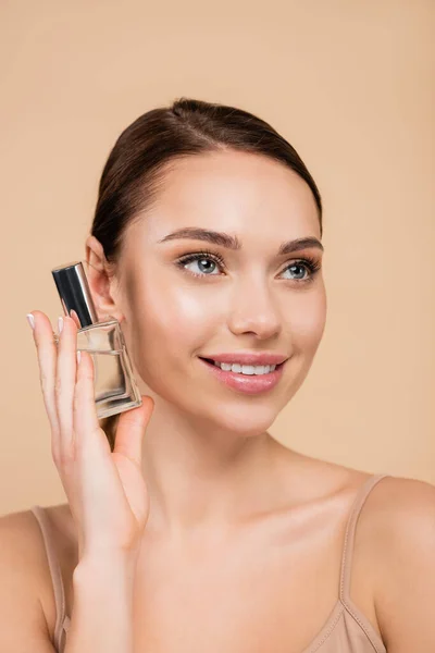 Mujer sonriente con rostro natural posando con perfume aislado en beige - foto de stock