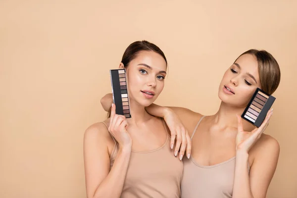 Jovem mulher apoiando-se no ombro do amigo segurando paleta sombras olho isolado no bege — Fotografia de Stock