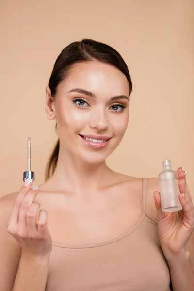 Mulher alegre segurando soro cosmético isolado no bege — Fotografia de Stock