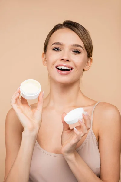 Femme heureuse avec crème cosmétique souriant à la caméra isolé sur beige — Photo de stock