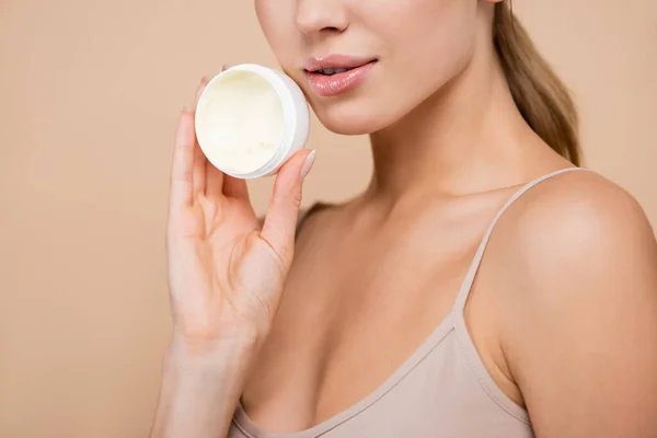 Vista cortada de mulher com lábios brilhantes segurando creme cosmético isolado no bege — Fotografia de Stock