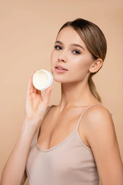 Young woman with perfect skin holding cosmetic cream isolated on beige — Stock Photo