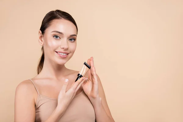 Jolie femme avec maquillage naturel tenant correcteur isolé sur beige — Photo de stock