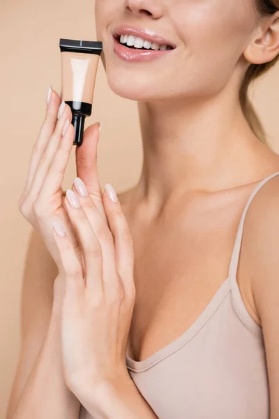 Cropped view of smiling woman holding tube of face foundation isolated on beige — Stock Photo