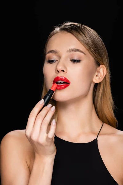 Bonita mujer aplicando lápiz labial rojo aislado en negro - foto de stock