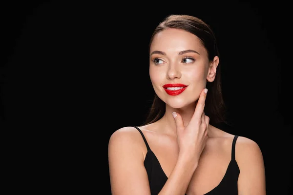 Donna gioiosa che tocca il viso, sorridendo e distogliendo lo sguardo isolato sul nero — Foto stock