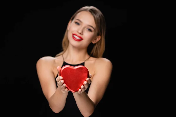 Messa a fuoco selettiva della scatola a forma di cuore nelle mani della donna offuscata isolata sul nero — Foto stock