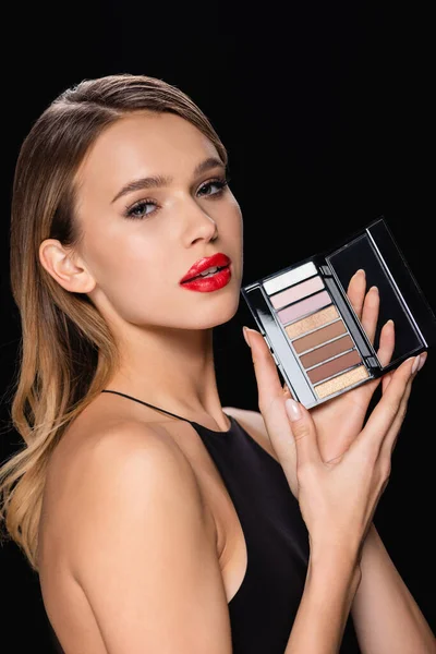 Pretty, young woman with eye shadows palette looking at camera isolated on black — Photo de stock
