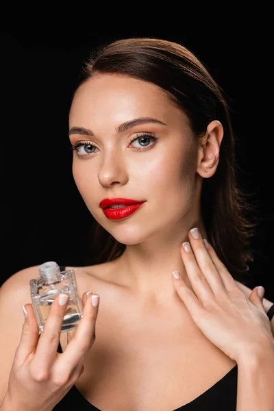 Bonita mujer aplicando perfume en el cuello aislado en negro — Stock Photo