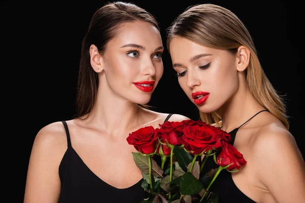 Giovane donna guardando affascinante amico con rose rosse isolate su nero — Foto stock