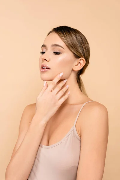 Young woman with perfect skin and natural makeup touching face isolated on beige — Photo de stock