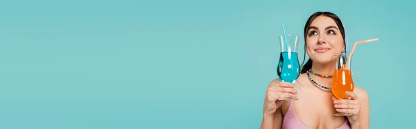 Mujer joven sonriendo mientras sostiene cócteles aislados en azul, pancarta - foto de stock