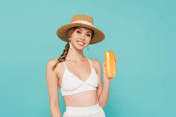 Smiling woman in straw hat holding sunscreen isolated on blue — Stock Photo
