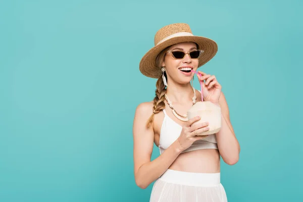 Fröhliche Frau mit Sonnenbrille hält Cocktail in Kokosnuss isoliert auf blau — Stockfoto