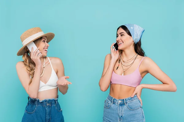 Mulheres positivas em tops falando em smartphones isolados em azul — Fotografia de Stock