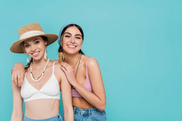 Smiling woman in top and bandana hugging friend isolated on blue — Stock Photo