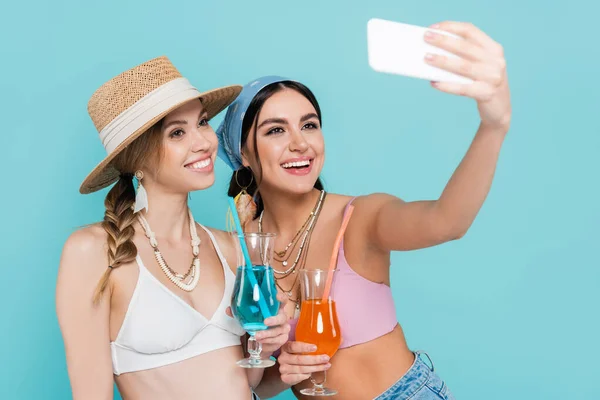 Amigos sorridentes no máximo segurando coquetéis e tirando selfie no smartphone isolado no azul — Fotografia de Stock