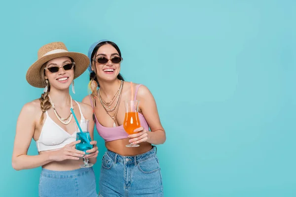 Donne sorridenti in occhiali da sole che tengono cocktail isolati su blu — Foto stock