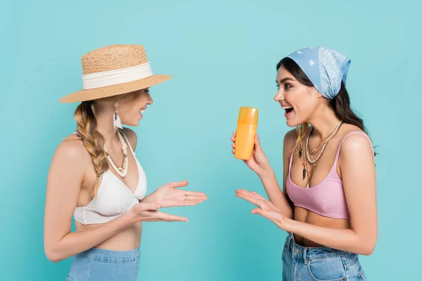 Smiling women in tops pointing at sunscreen isolated on blue — Stock Photo