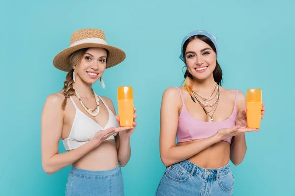 Pretty women in tops pointing at sunscreen isolated on blue — Stock Photo