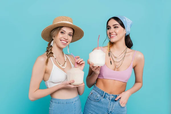 Mulheres bonitas em tops segurando coquetéis em cocos isolados em azul — Fotografia de Stock