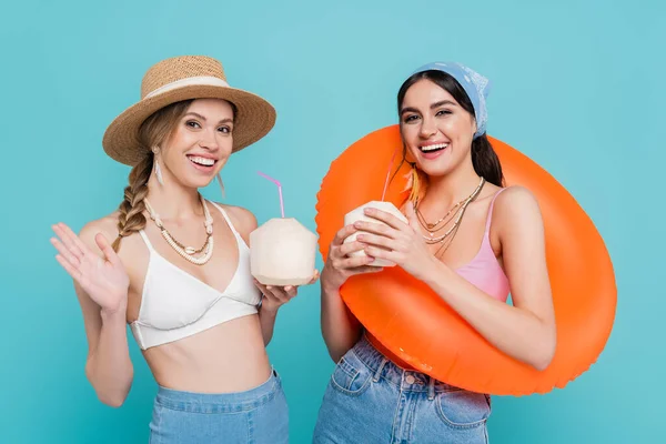 Amigos alegres con cócteles en cocos y anillo de natación aislado en azul - foto de stock