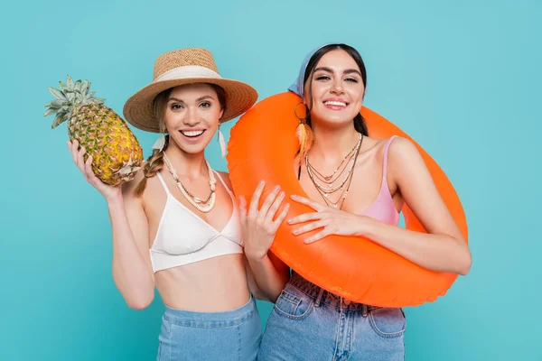 Smiling women holding swim ring and pineapple isolated on blue — Stock Photo