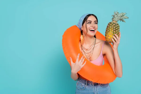 Весела жінка з плавальним кільцем тримає ананас ізольовано на синьому — стокове фото