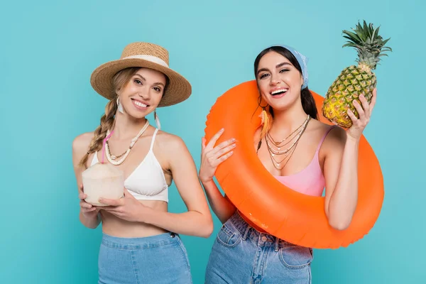 Smiling friends with pineapple and swim ring isolated on blue — Stock Photo