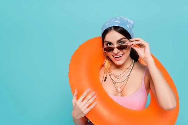 Весела жінка в сонцезахисних окулярах тримає плавальний кільце ізольовано на синьому — стокове фото