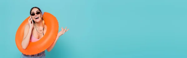 Щаслива жінка з плавальним кільцем розмовляє на смартфоні ізольовано на синьому, банер — стокове фото