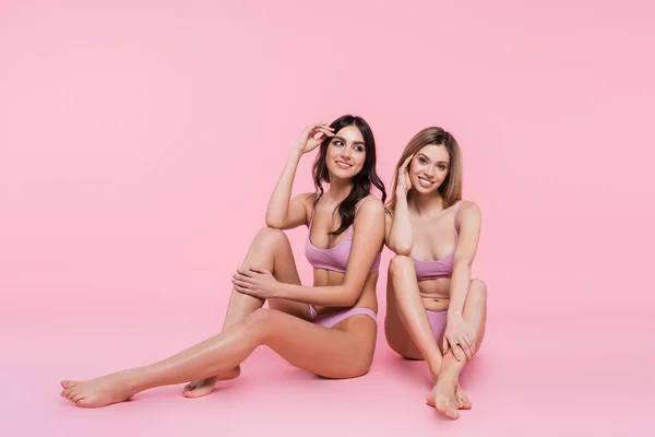 Mujeres jóvenes en trajes de baño sentadas sobre fondo rosa - foto de stock