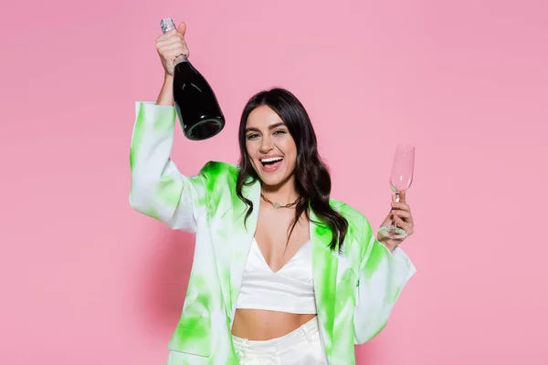 Mulher positiva segurando garrafa de champanhe no fundo rosa — Fotografia de Stock