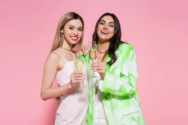 Pretty friends with champagne smiling at camera on pink background — Stock Photo