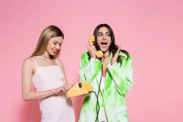 Улыбающаяся женщина держит телефон рядом взволнованный друг разговаривает на розовом фоне — стоковое фото