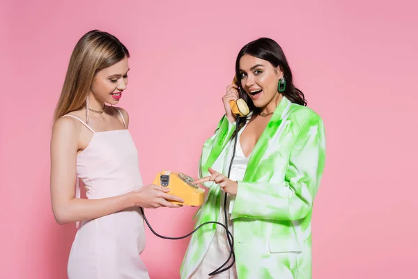 Mujer sonriente hablando por teléfono cerca de un amigo sobre fondo rosa - foto de stock