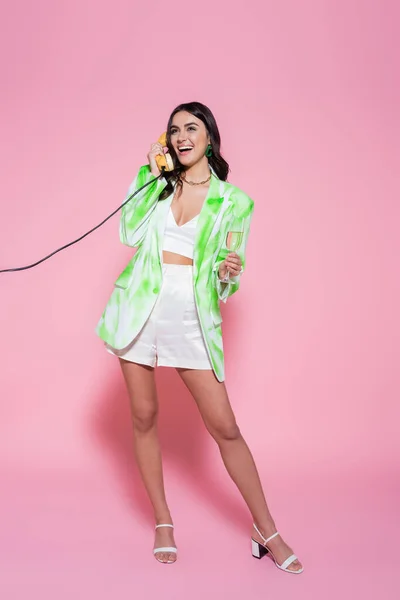 Mulher feliz com copo de champanhe falando por telefone no fundo rosa — Fotografia de Stock