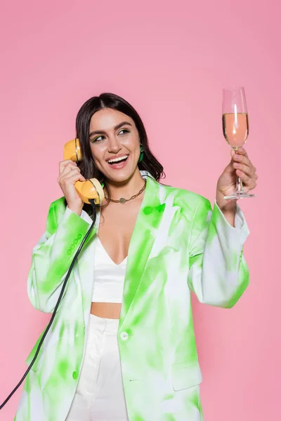 Pretty woman talking on telephone and holding glass of champagne isolated on pink — Stock Photo