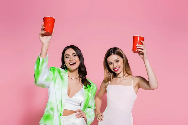 Cheerful friends holding plastic cups on pink background — Stock Photo