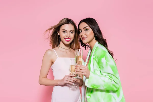 Mujeres bonitas sosteniendo copas de champán sobre fondo rosa - foto de stock