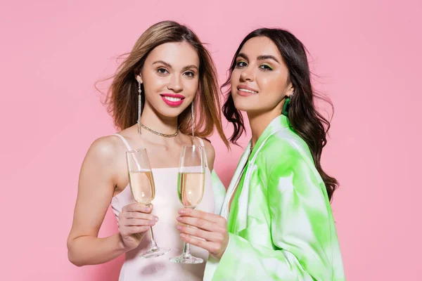 Amigos sonrientes sosteniendo copas de champán y mirando a la cámara sobre fondo rosa - foto de stock
