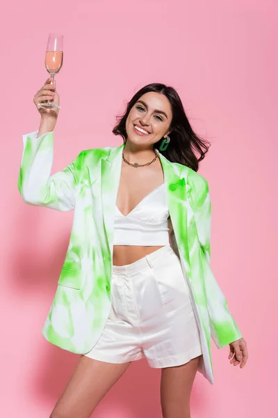 Brunette woman in stylish clothes holding champagne on pink background — Stock Photo