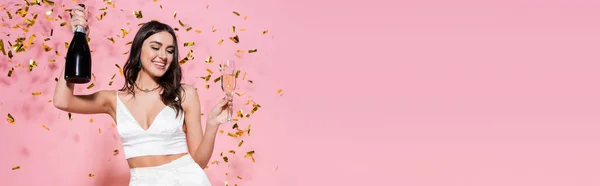Stylish woman with champagne near festive confetti on pink background, banner — Stock Photo