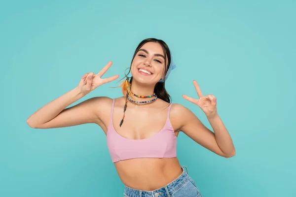 Mujer sonriente en la parte superior y bandana mostrando la paz aislada en azul - foto de stock