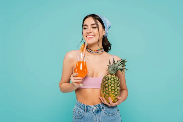 Mulher sorridente bebendo coquetel e segurando abacaxi isolado em azul — Fotografia de Stock