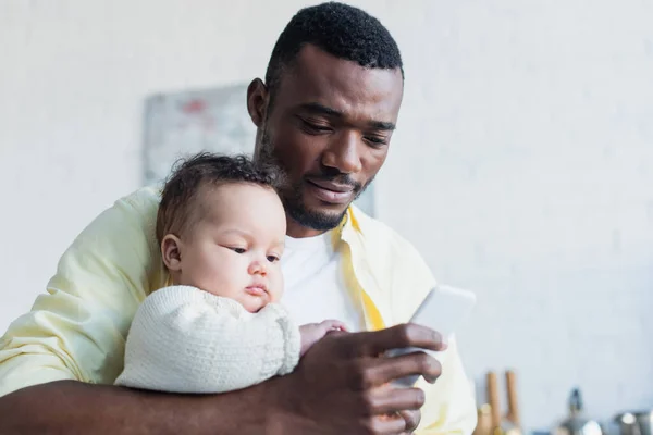 Africano americano hombre celebración pequeño hija mientras charlando en celular - foto de stock