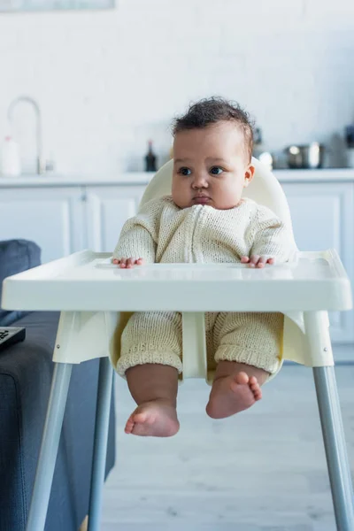 Africano americano bebé niño sentado en silla de bebé en cocina - foto de stock