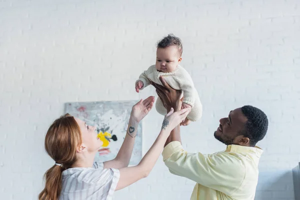 African american man raising infant child near wife at home — Stock Photo